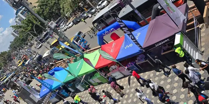 Colorful vendor tents line a busy city street during an outdoor event, with a crowd walking along the sidewalk.